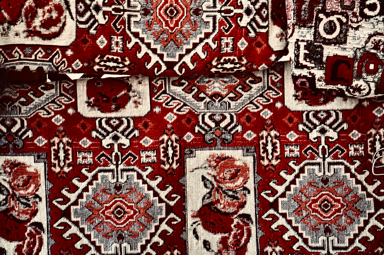 Menu Close-up of a handmade carpet showcasing detailed red and white traditional patterns, emphasizing handcraft.