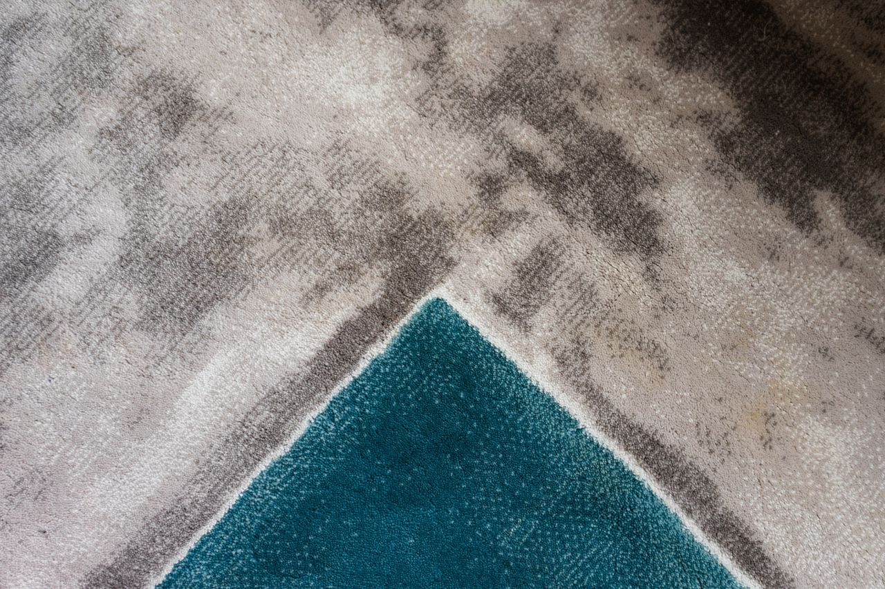 Close-up of a modern geometric carpet texture with teal and gray hues.