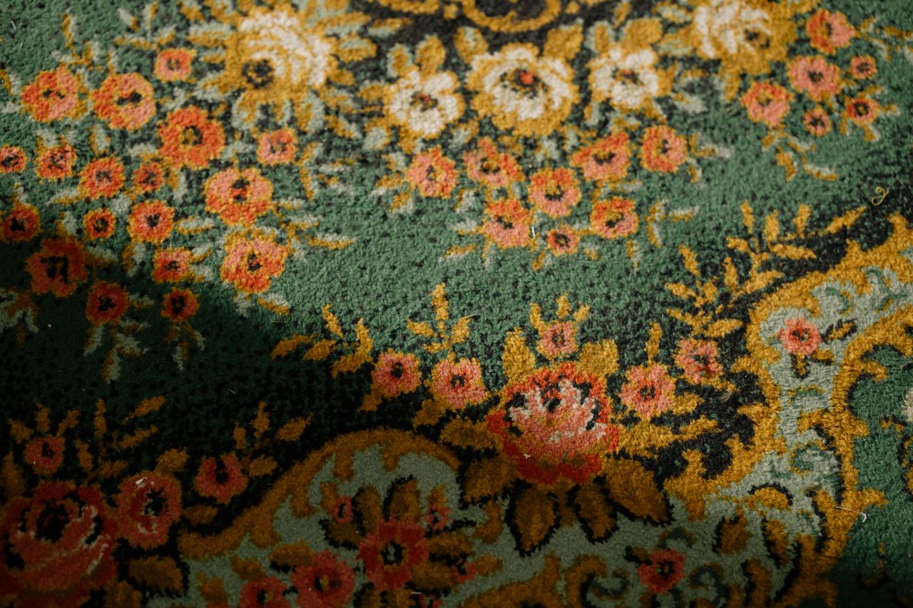 Close-up of a vintage floral patterned carpet with intricate textures and warm colors.
