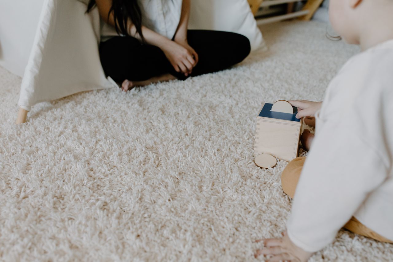 Menu A child plays with a wooden block toy on a cozy carpet indoors, creating a warm family moment.