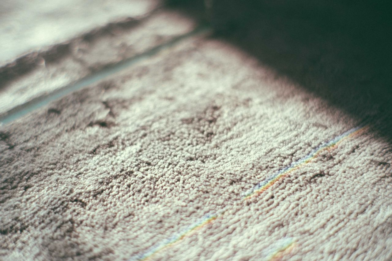 Menu Closeup of gray textured carpet with thin colorful lines placed on floor in room with bright sunlight and shadow at home