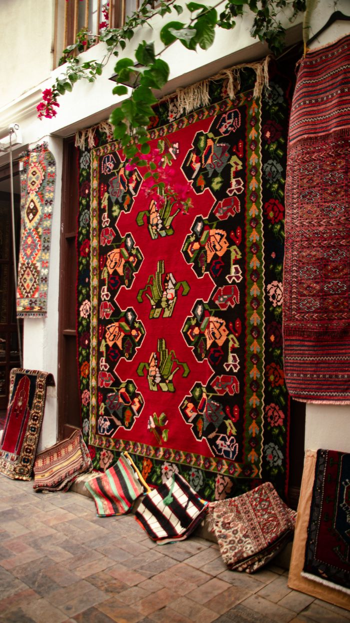 Vibrant traditional rugs and carpets on display outdoors, showcasing intricate patterns and rich colors.